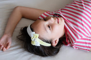 Model with double knot bow headband in pale green-yellow and white.